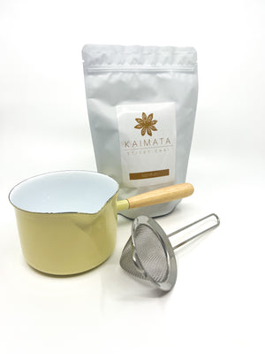 A packet of organic Sticky Chai Tea with a strainer and enamelware chai brewing pot